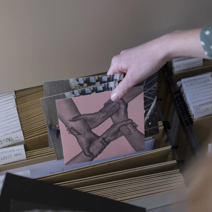 Une main tient des reproductions d'oeuvres d'art rangées dans un meuble de classement