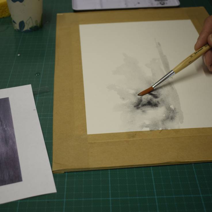 Eine Hand hält einen Pinsel und malt auf ein Blatt Papier