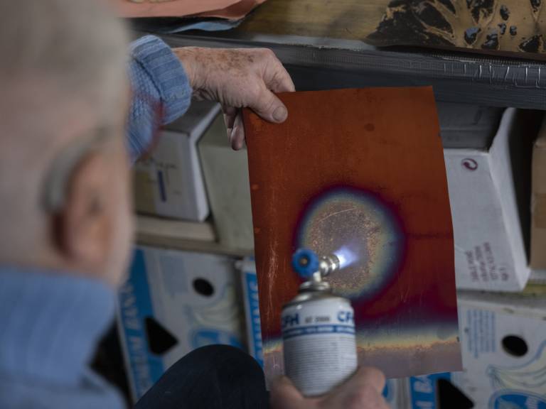 Arthur Unger brennt eine runde Form in eine Kupferplatte mithilfe eines Gasbrenners